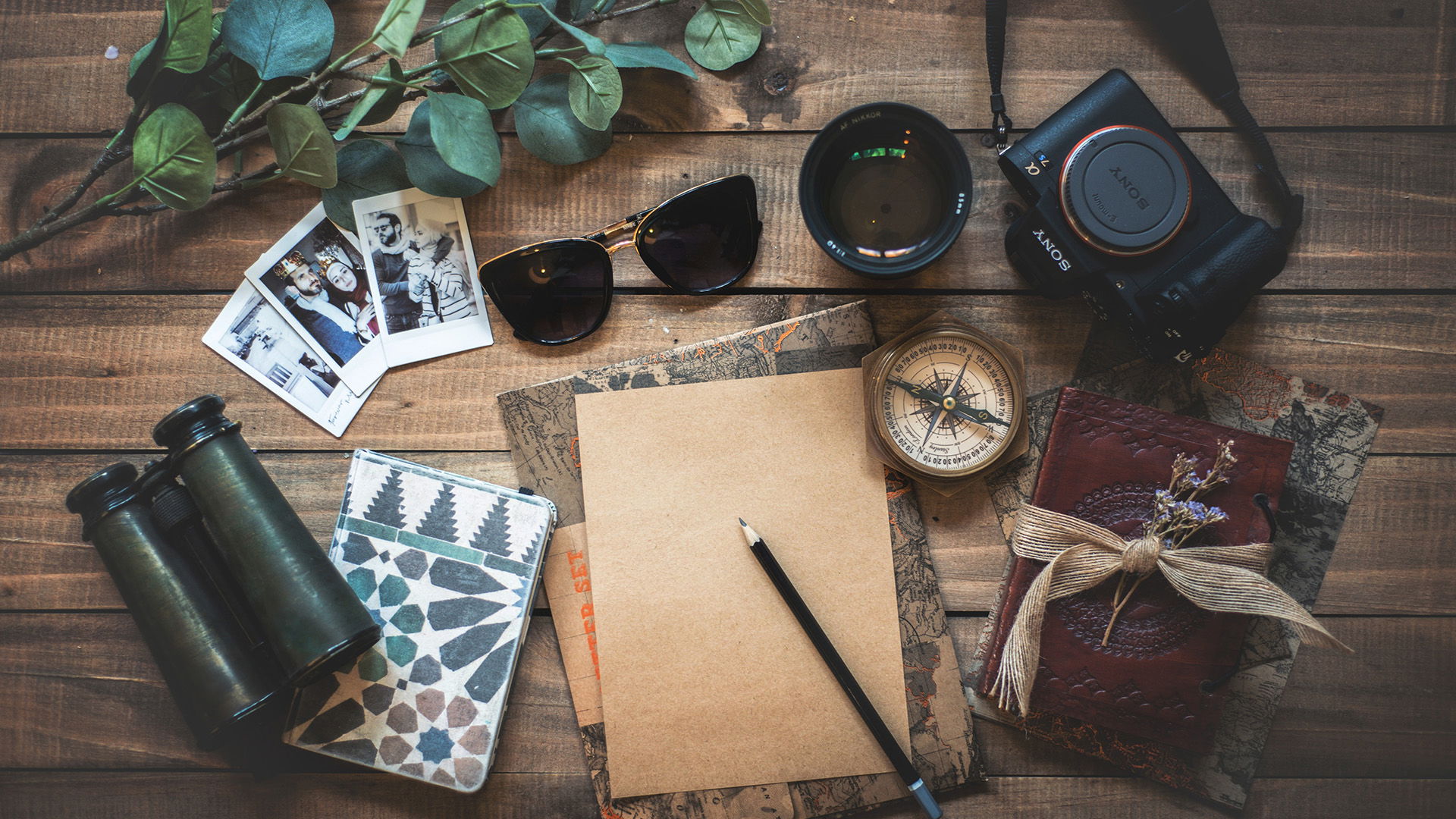 A table, pictured from above, laid out with a compass, sunglasses, maps, pencils and other travel related items